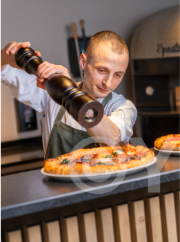 Pizzaiolo im Hotel Krone würzt Pizza mit Pfeffer
