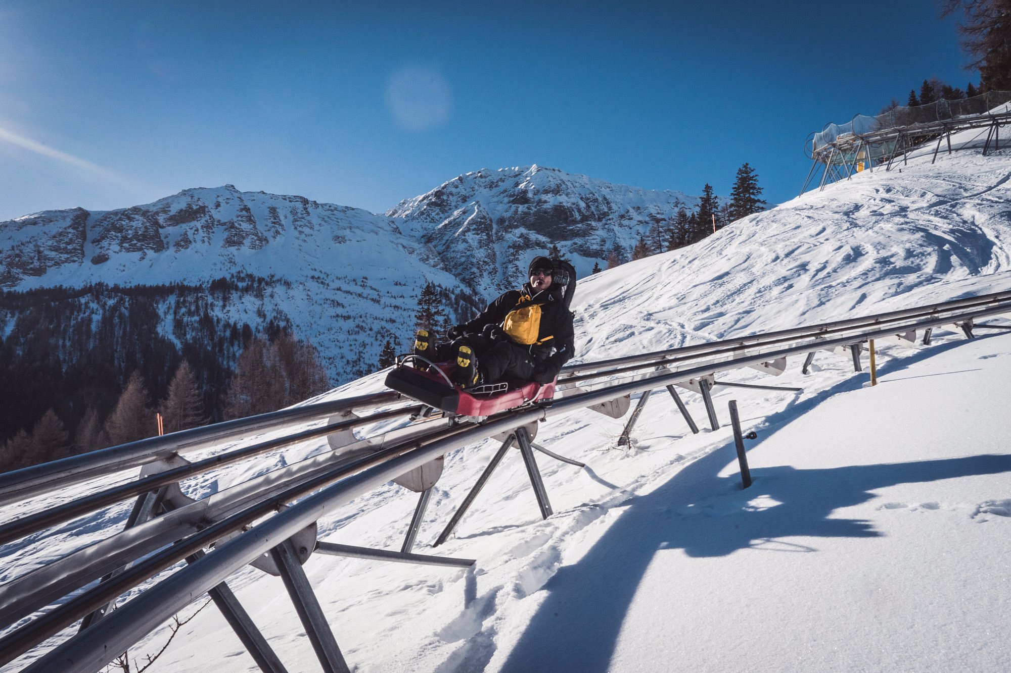 Mann fährt mit der Rodelbahn durch die Winterlandschaft am Erlebnisberg Pradaschier in Churwalden