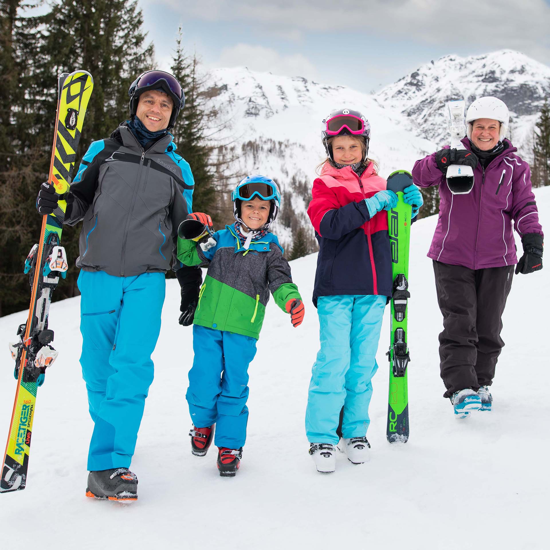 Eine Familie mit zwei Kindern steht in Skiausrüstung da und hält ihre Ski in der Hand