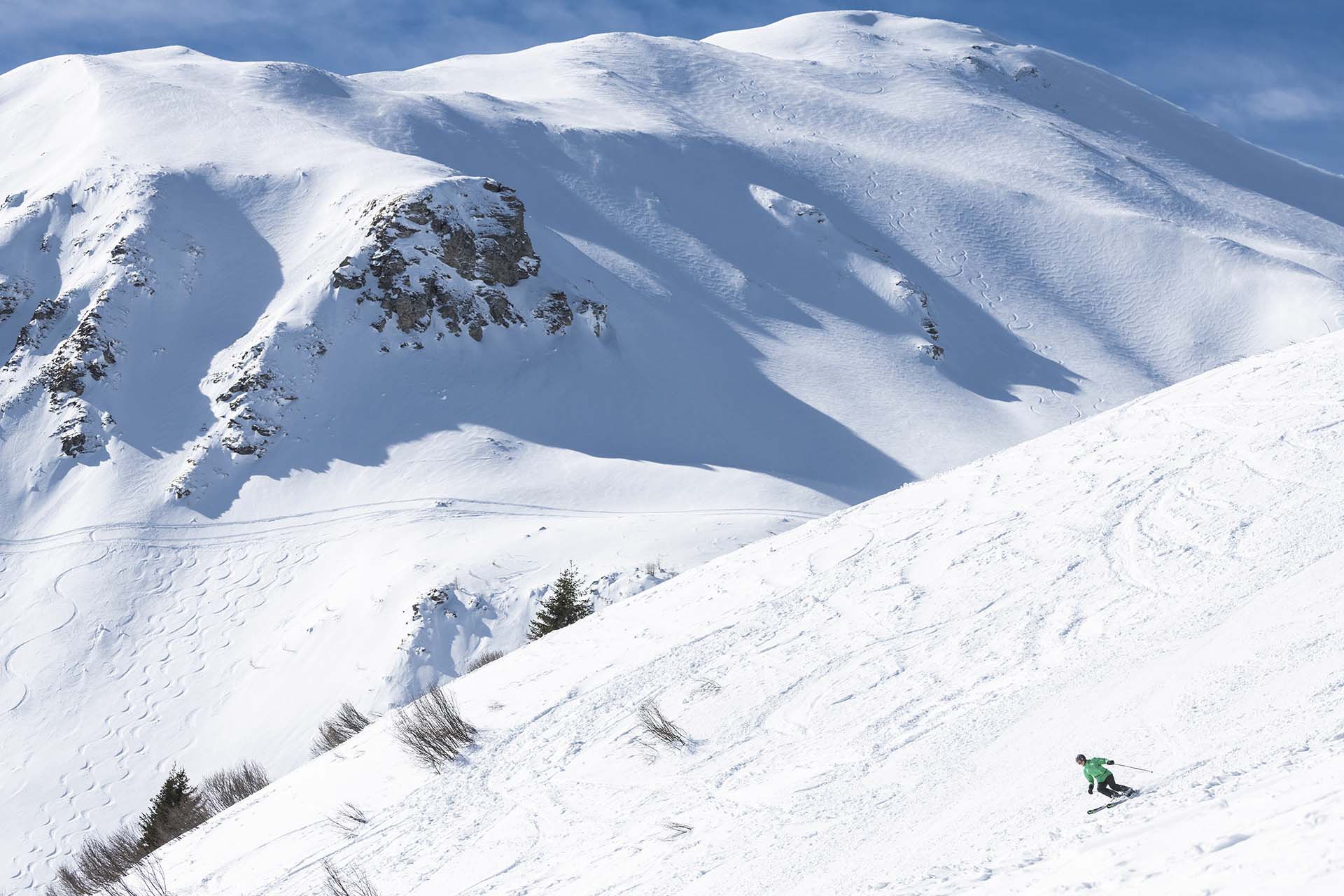 Ein Skifahrer mit gruener Jacke genießt die Abfahrt auf der Piste auf dem Erlebnisberg in Pradaschier bei schoenem Wetter