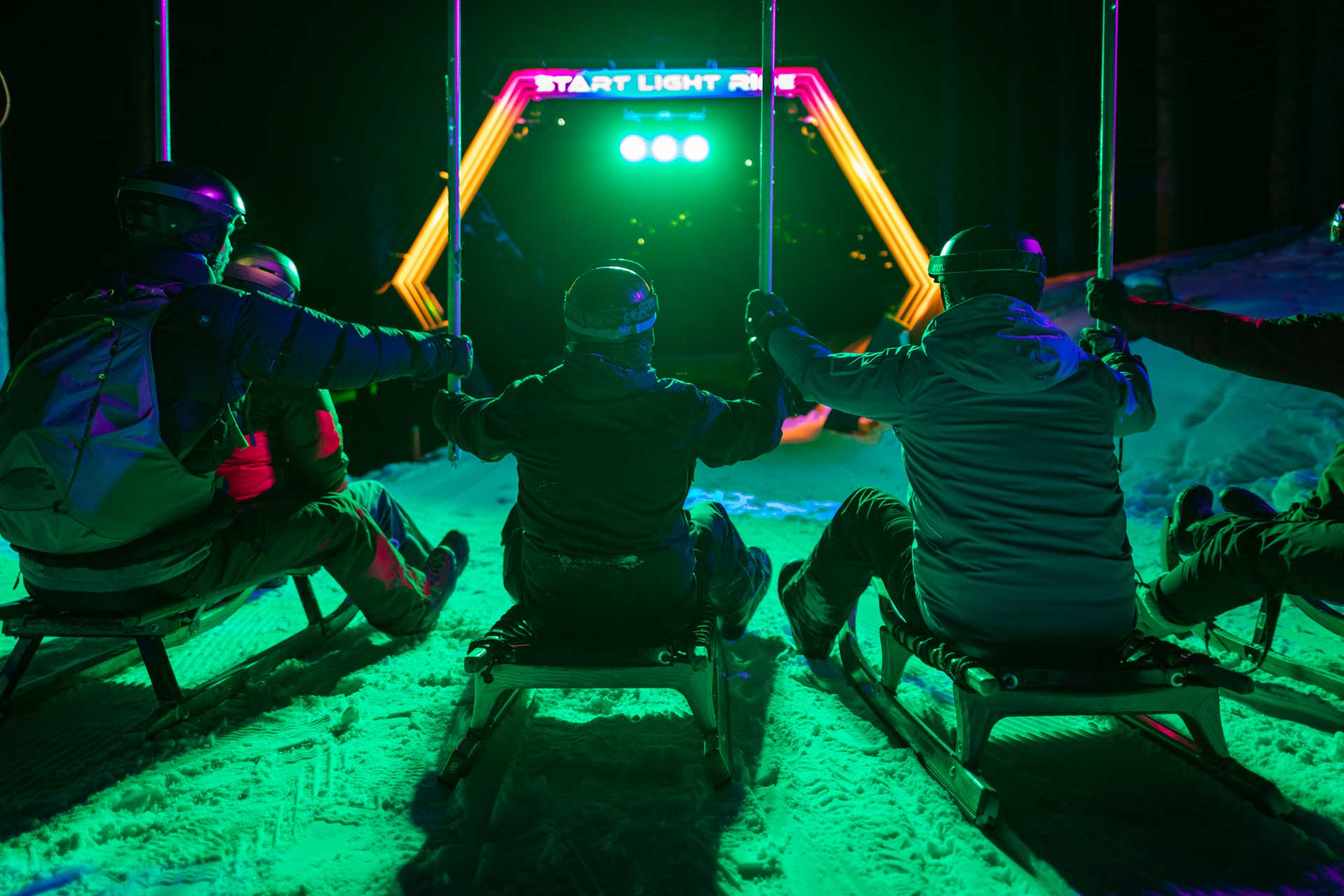 Eine Gruppe Freunde rodelt beim Nachtschlittelerlebnis Light Ride in der Lenzerheide